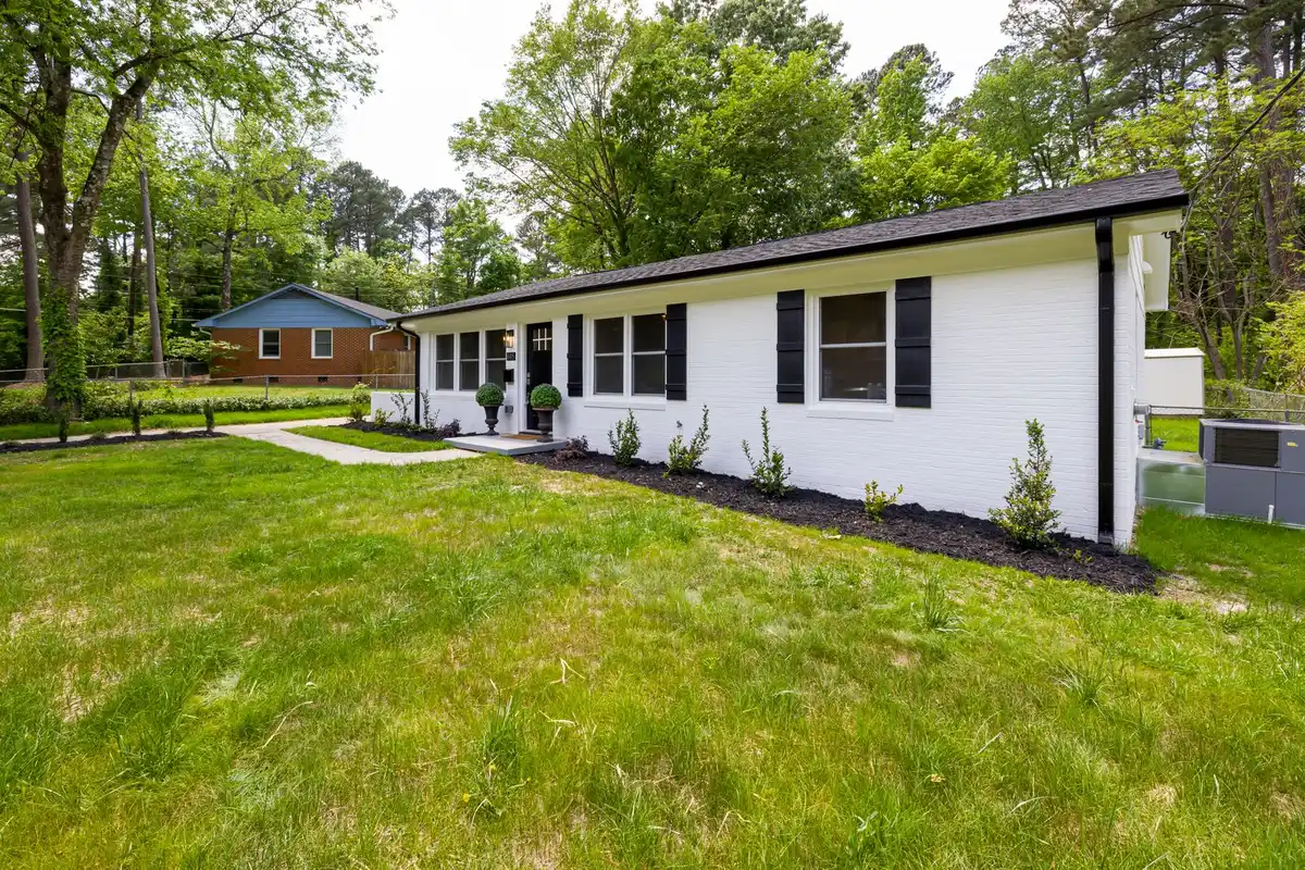 Suburban brick ranch home with a lawn and trees behind it