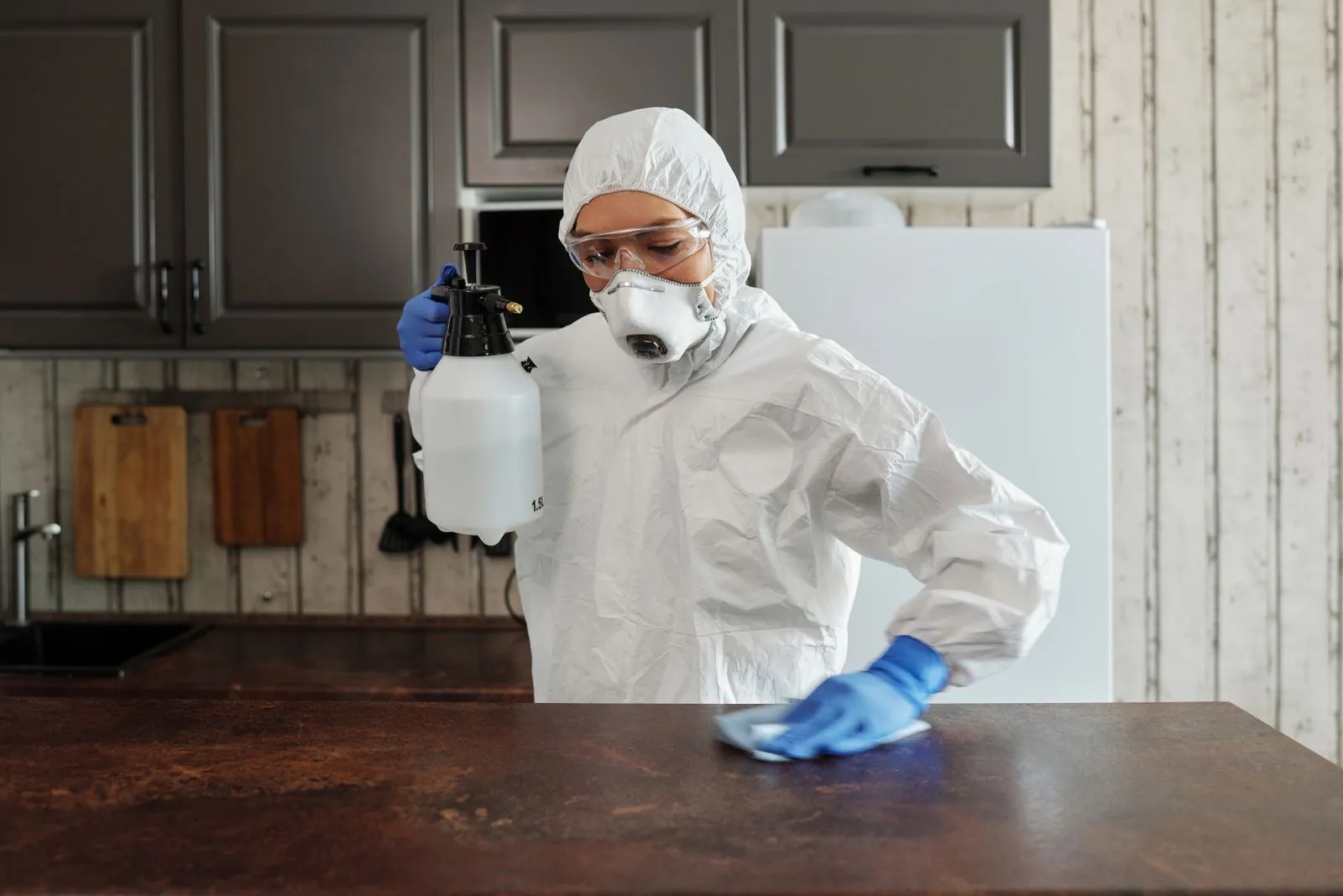 Pest control technician in work clothes treating along a kitchen baseboard