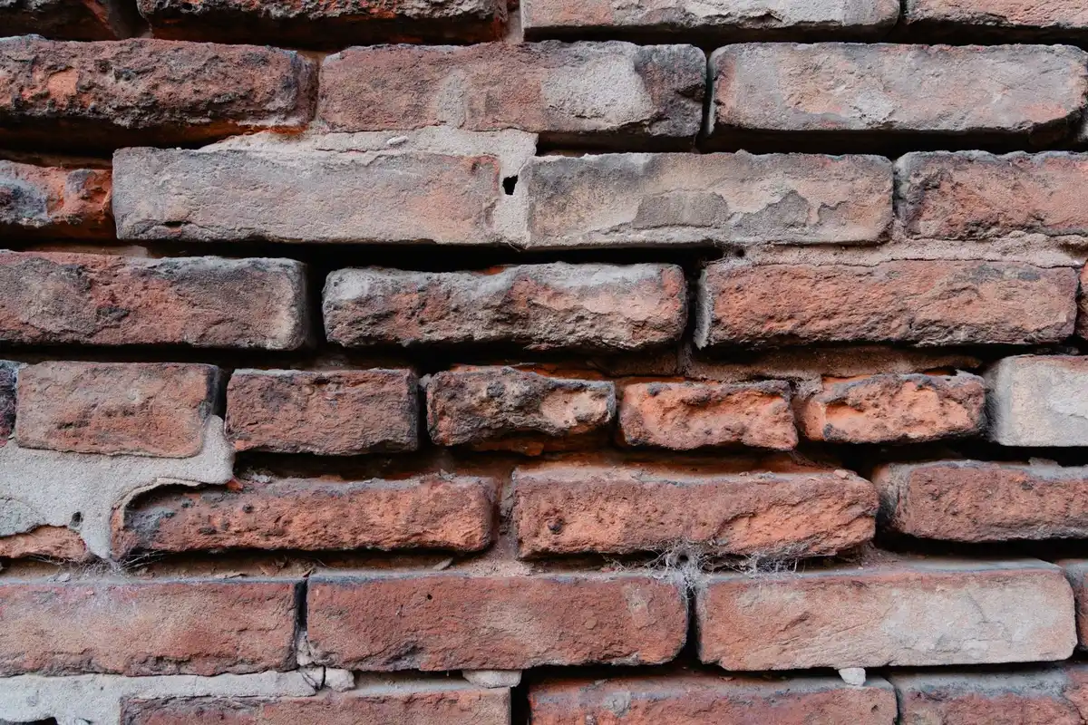 Pest control technician sealing a gap at the base of a brick house with sealant