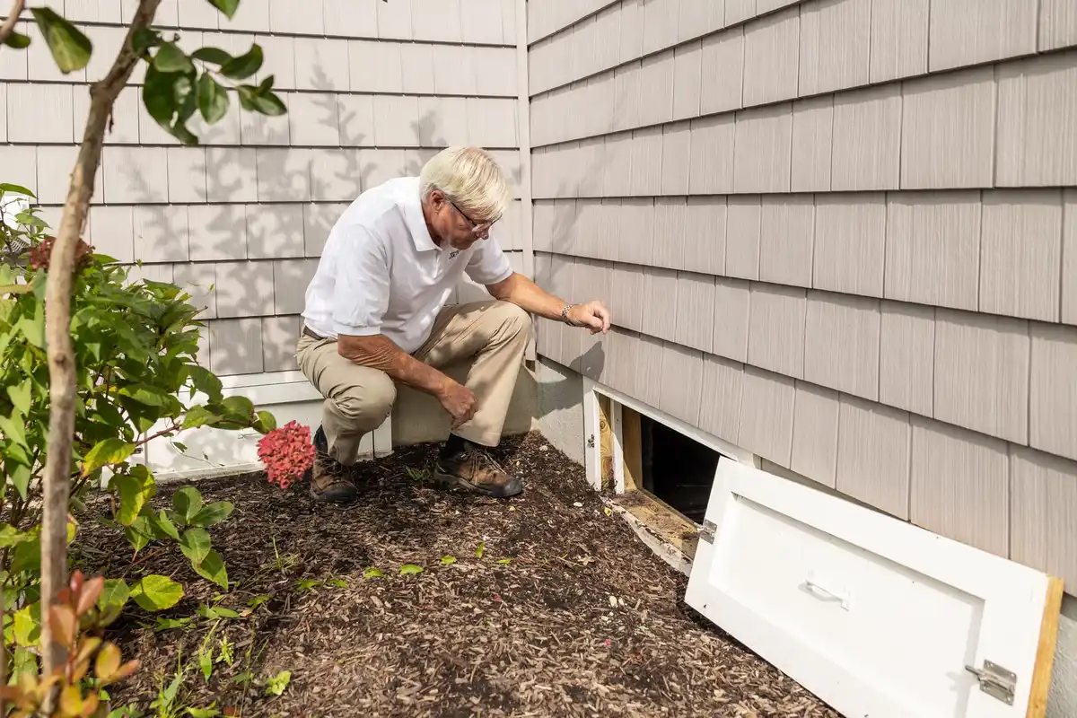 Inspector using a flashlight to check floor joists in a crawlspace